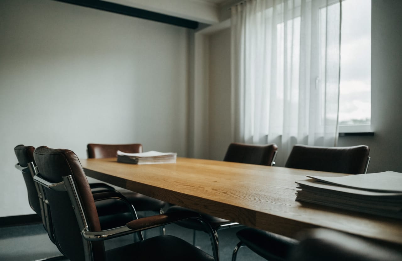 Empty meeting room with a long wooden table, leather chairs and stacks of files